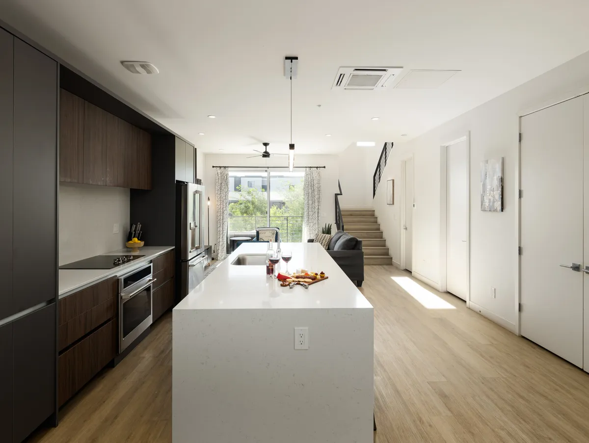 A modern kitchen and dining area featuring a kitchen island with stainless steel appliances, a dining table, and a staircase leading to an upper floor. The space is designed for entertaining, cooking, and sharing meals, with a warm, contemporary feel.