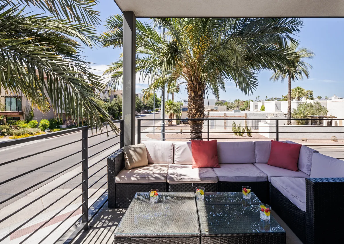 A serene patio featuring outdoor seating, a palm tree, and a coffee table with drinks, set against a peaceful backdrop. The arrangement encourages group conversations, quiet coffee breaks, or casual social events under the open sky.