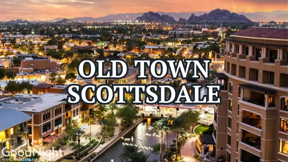 A vibrant evening scene of Old Town Scottsdale featuring the iconic sign, a picturesque waterway, illuminated buildings, and a stunning mountain backdrop. The image captures people strolling along the water and dining at outdoor cafes, with the area bathed in inviting lights and sunset colors.