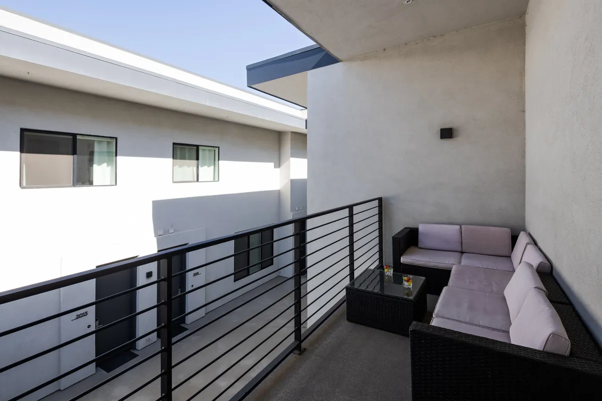 A contemporary balcony with comfortable seating, a glass table, and views of the surrounding architecture. The space is ideal for enjoying drinks or casual gatherings with friends, bridging the excitement of the city with the comfort of home.