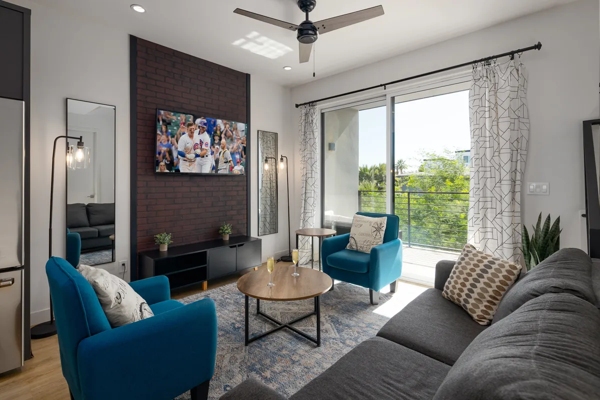 The image showcases a cheerful and relaxed living area with plush blue armchairs, a stylish wooden coffee table, and a large television broadcasting a live sports event. The space is inviting for socializing, enjoying drinks, or gathering for a cozy movie night.