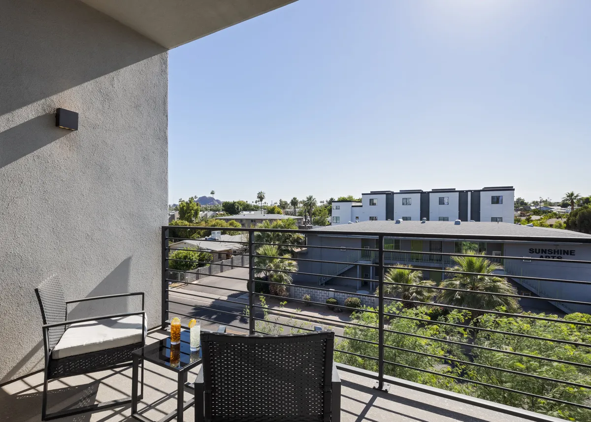 A calm balcony with chairs overlooking a lively street and surrounding area, creating an inviting spot to enjoy the view, sip drinks, or host small gatherings. The urban backdrop connects the property to the city’s vibrant atmosphere.